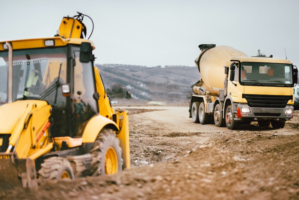 Industrial backhoe excavator machinery and cement truck on road construction site