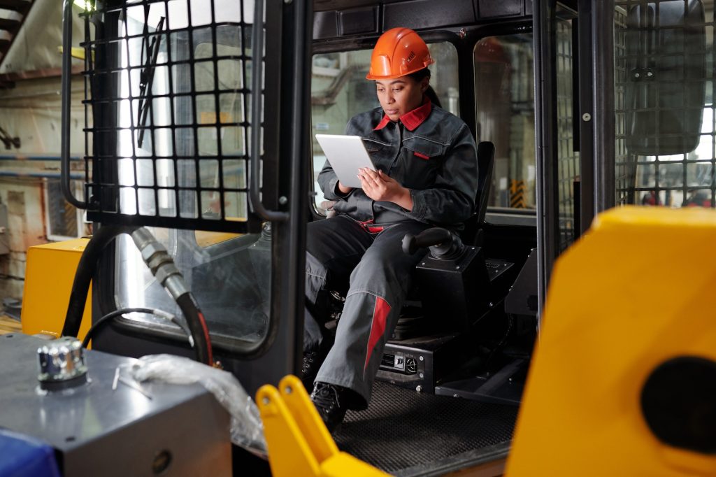 Young busy worker of factory scrolling in tablet in construction machine